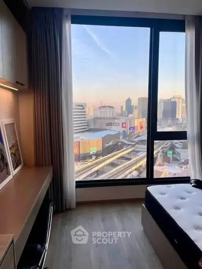 Modern bedroom with city view from large window, featuring a cozy workspace and stylish decor.