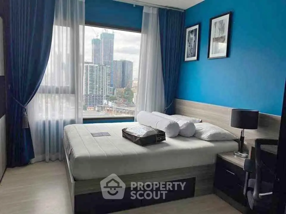 Modern bedroom with city view, blue accent wall, and stylish decor in urban apartment.