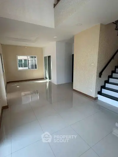 Spacious modern living room with glossy tile flooring and staircase, perfect for family gatherings.