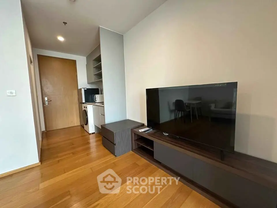 Modern living room with wooden flooring, TV, and compact kitchen area in a stylish apartment.