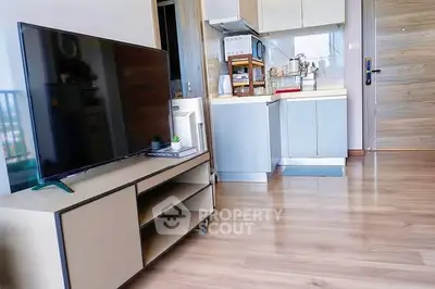 Modern living room with sleek TV stand and compact kitchen in open layout apartment.