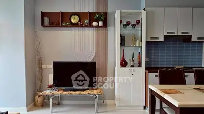 Modern living room with stylish decor and open kitchen layout, featuring sleek furniture and elegant shelving.