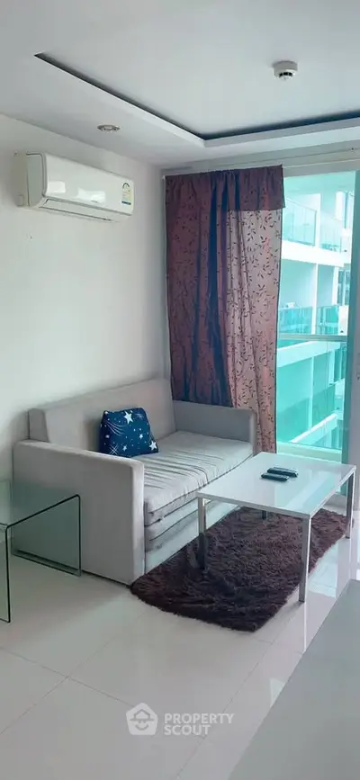Modern living room with sleek sofa, glass table, and balcony view in a stylish apartment.