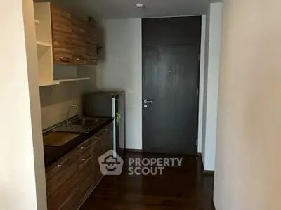 Compact kitchen with wooden cabinets and small fridge in modern apartment