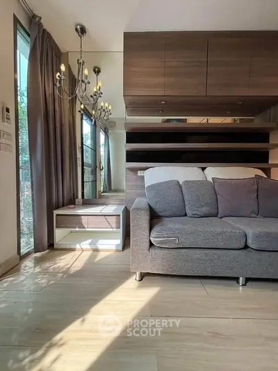 Modern living room with elegant chandelier and cozy sofa, featuring large windows and stylish wooden accents.