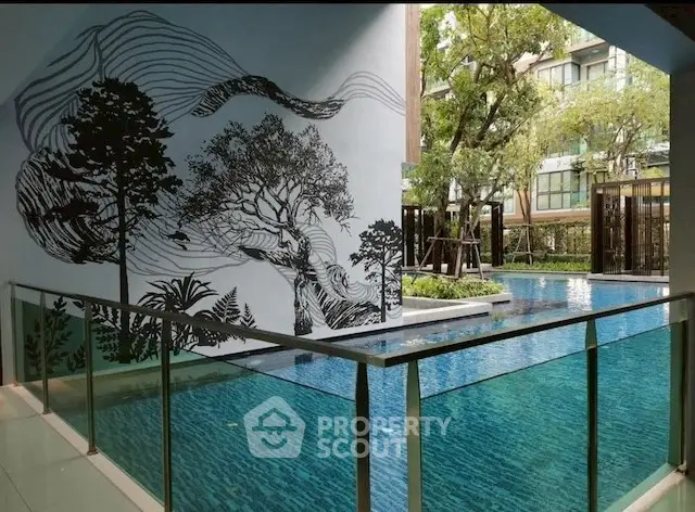 Modern apartment pool with artistic wall mural and lush greenery.