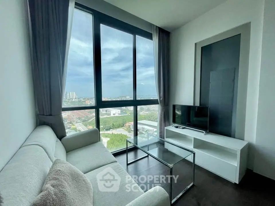 Modern living room with large windows offering stunning city views, featuring a cozy sofa and sleek TV setup.