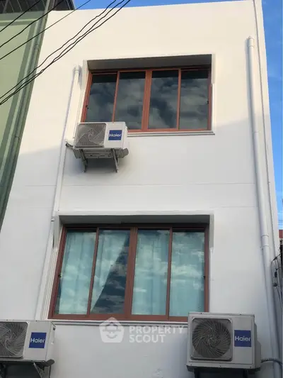 Modern building exterior with air conditioning units and large windows reflecting the sky.