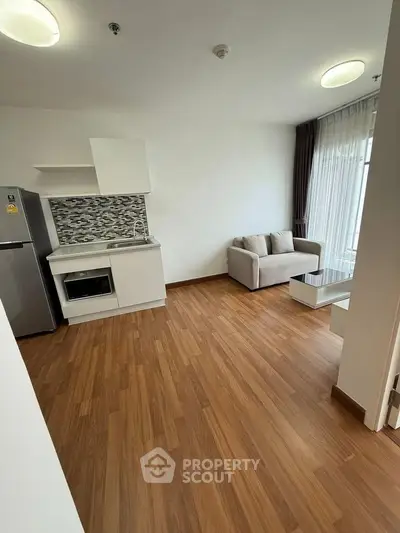 Modern open-layout living room with sleek kitchen and cozy seating area, featuring wooden flooring and natural light.
