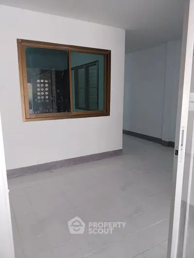 Spacious unfurnished room with tiled flooring and large window, ideal for customization.