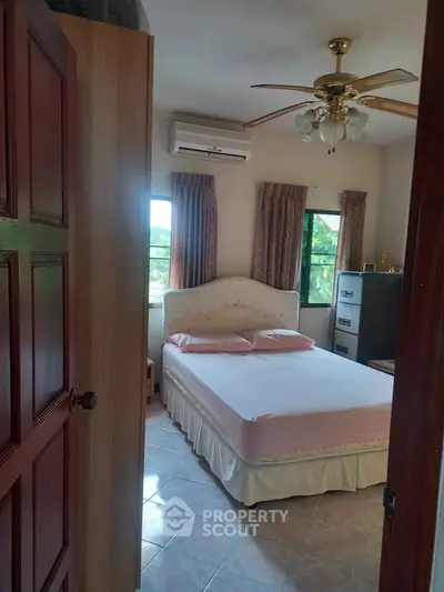 Cozy bedroom with ceiling fan and air conditioning, featuring a comfortable bed and natural light.