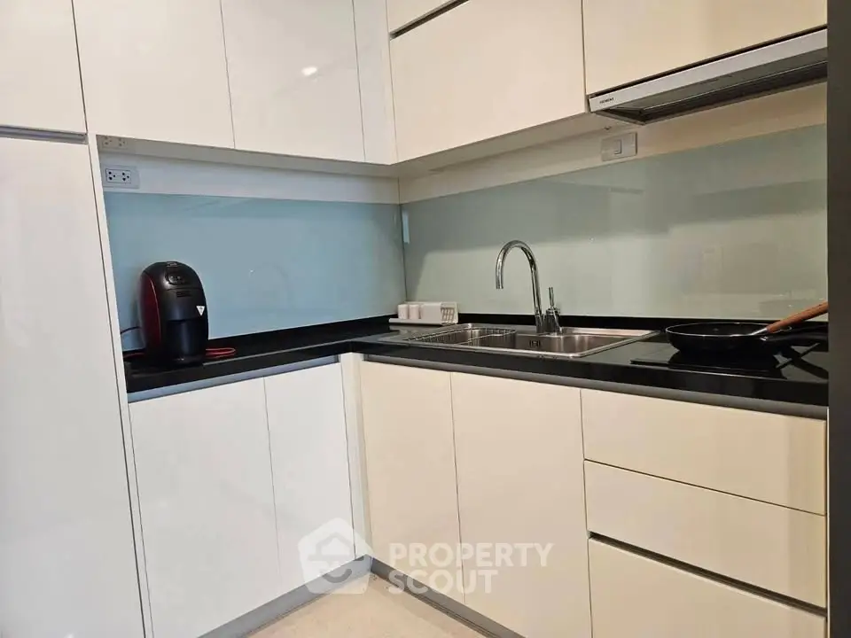 Modern kitchen with sleek white cabinets and black countertops, featuring a coffee maker and stainless steel sink.
