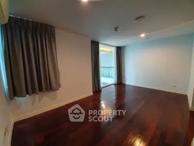 Spacious empty room with polished wooden floors and large windows, ideal for customization.