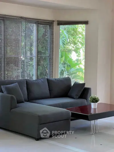 Spacious living room with modern sofa and large windows offering lush garden views.