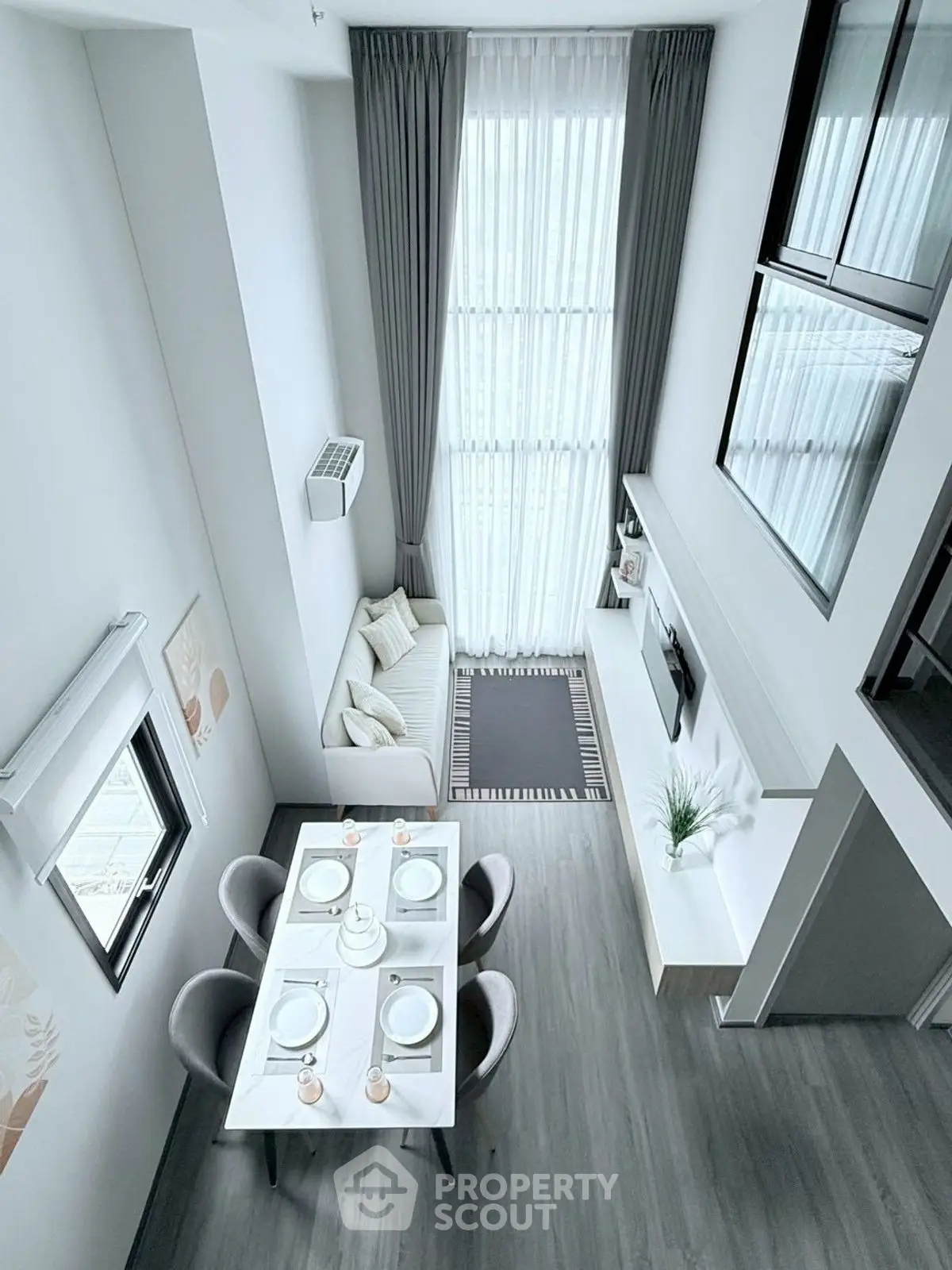 Modern living room with high ceilings and elegant dining area, featuring large windows and stylish decor.