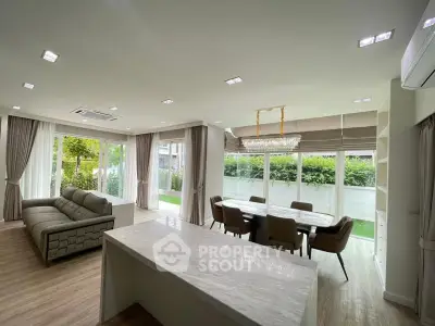 Spacious open-plan living and dining area with modern furnishings and large windows overlooking a lush garden.