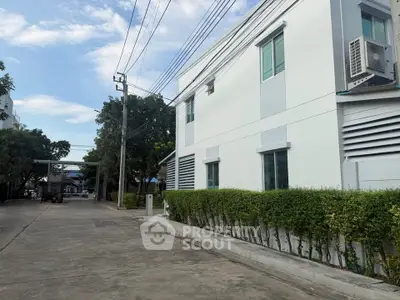 Modern white building exterior with lush greenery and clear blue sky.