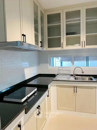 Modern kitchen with sleek cabinetry and black countertops, featuring a built-in stove and ample storage space.