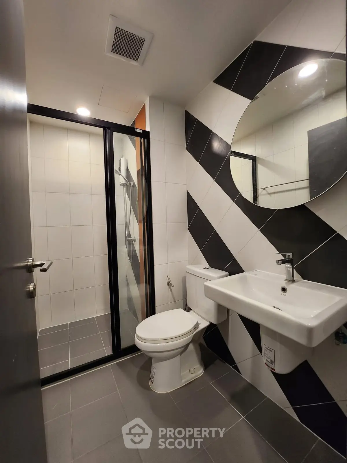 Modern bathroom with sleek design featuring a glass shower, round mirror, and stylish black and white tiles.