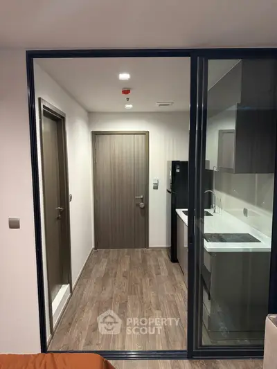 Modern kitchen with sleek appliances and wooden flooring in a compact apartment.