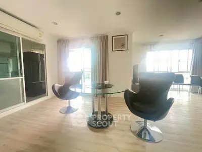 Modern living room with stylish chairs and glass table, featuring large windows for natural light.