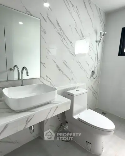 Modern bathroom with sleek fixtures and elegant marble tiles, featuring a stylish sink and toilet.