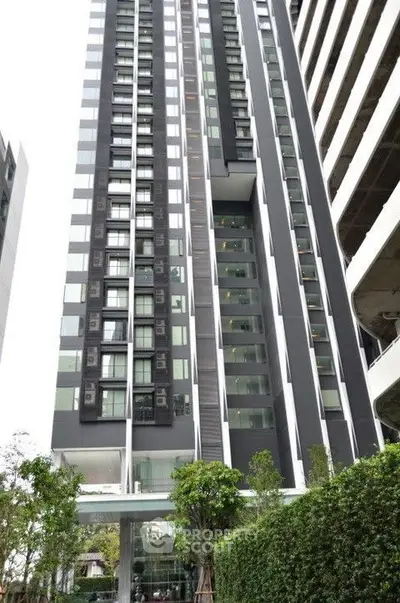 Modern high-rise building exterior with sleek design and lush greenery.
