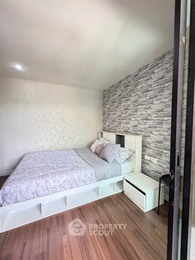 Modern bedroom with stylish stone accent wall and cozy bedding in a well-lit space.