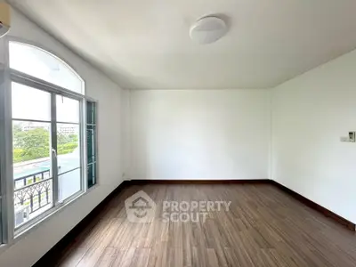 Spacious empty room with large window and wooden flooring, perfect for customization.