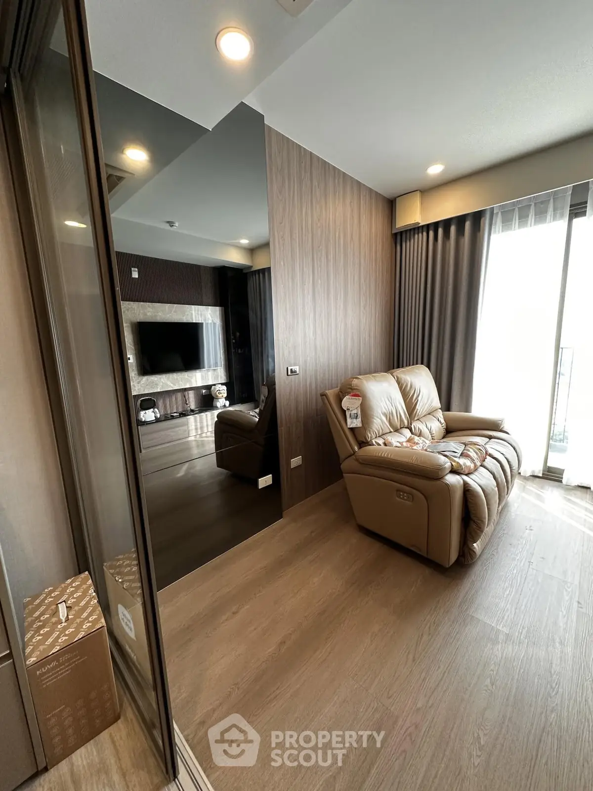 Modern living room with cozy leather sofa and large TV, featuring elegant wood flooring and stylish decor.