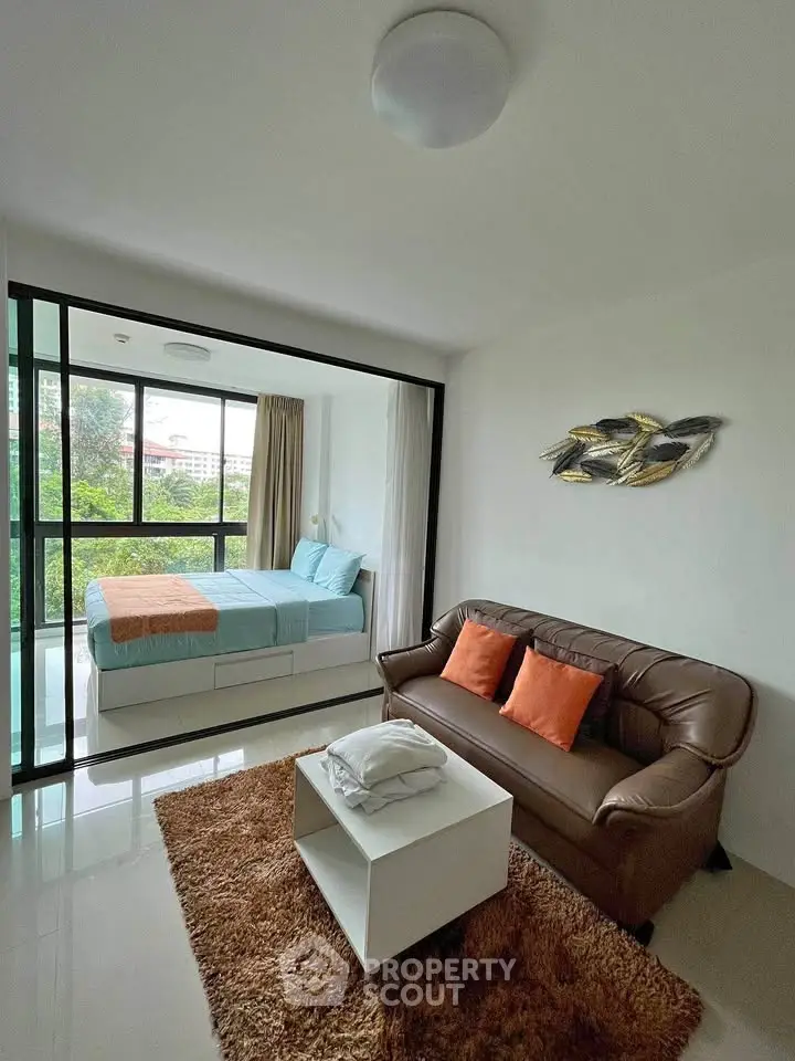 Modern studio apartment with cozy living area and large windows offering lush green views.