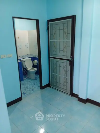 Cozy blue-tiled bathroom with secure metal door and modern fixtures, perfect for compact living spaces.