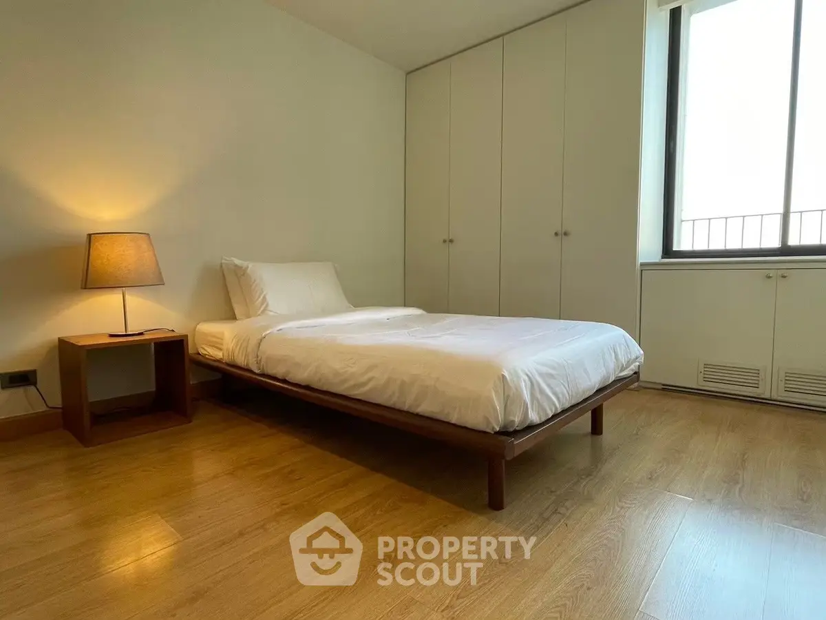 Spacious bedroom with wooden flooring and minimalist design, featuring a cozy bed and ample storage.