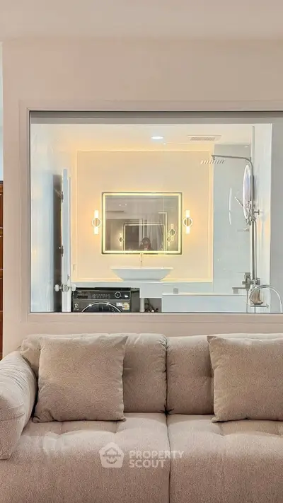 Modern interior with a cozy sofa and a view into a stylish bathroom featuring a washing machine.