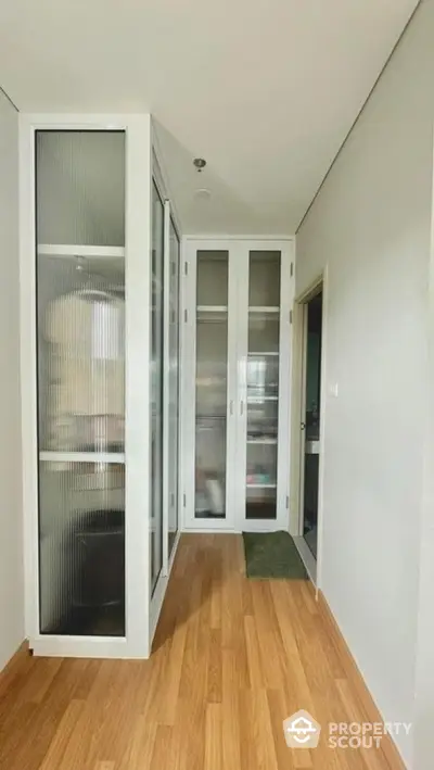 Modern hallway with wooden flooring and glass-paneled storage doors