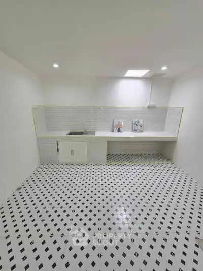 Minimalist kitchen with white tiled flooring and backsplash, featuring a sleek countertop and sink.