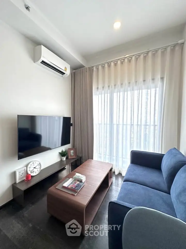 Modern living room with sleek furniture and natural light, featuring a wall-mounted TV and air conditioning.