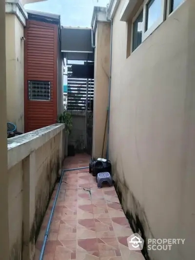 Narrow exterior passageway with tiled flooring and adjacent building walls.