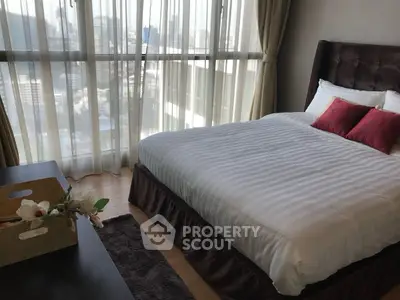 Cozy bedroom with large windows offering stunning city views, featuring elegant decor and plush bedding.