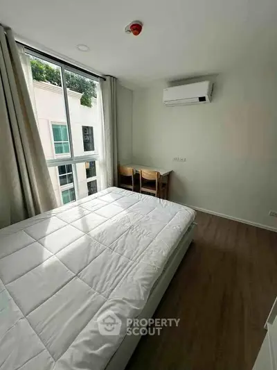 Bright bedroom with large window, modern air conditioning, and cozy wooden furniture in a stylish apartment.