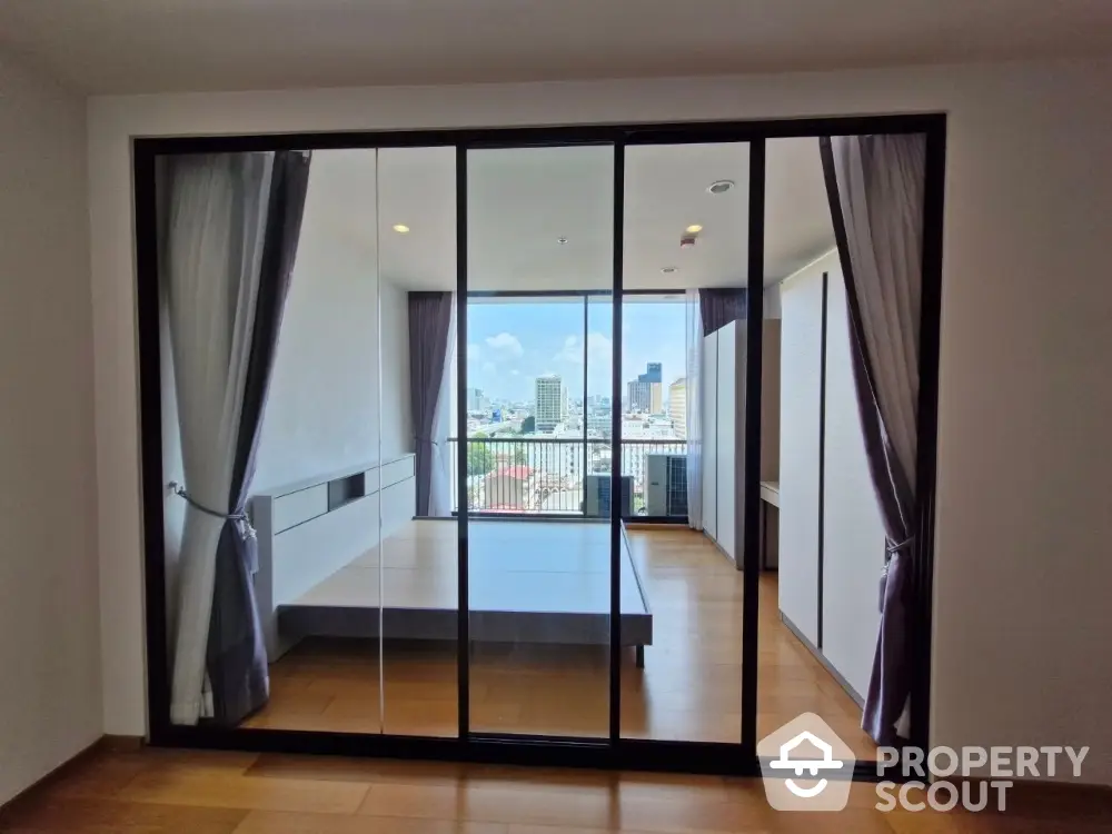 Modern bedroom with floor-to-ceiling windows and city view, featuring elegant wooden flooring and stylish curtains.