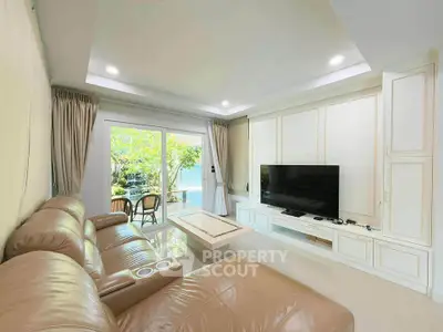 Spacious living room with leather sofa and large TV, opening to a lush garden view.