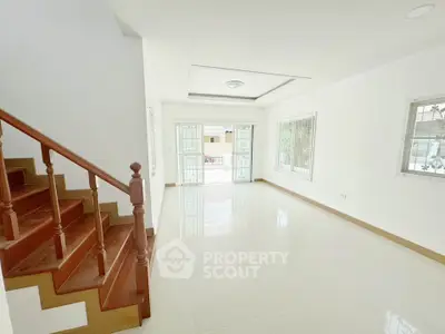 Spacious and bright living room with elegant wooden staircase and large windows.