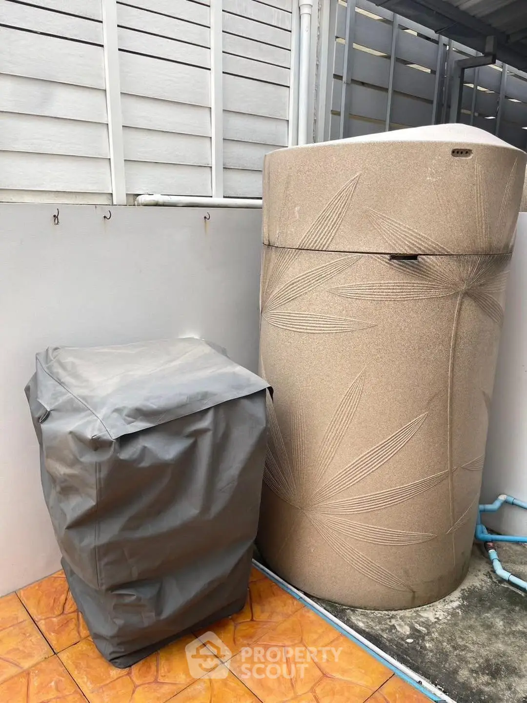 Outdoor utility area with large water tank and covered unit on tiled floor.