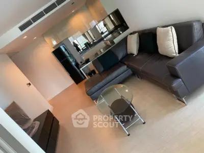 Modern living room with sleek leather sofa and glass coffee table in open layout apartment.