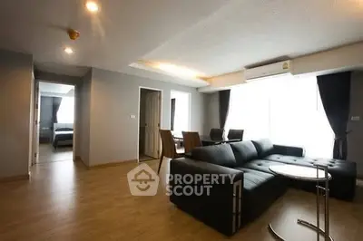 Spacious modern living room with sleek black sofa and dining area, featuring large windows for natural light.