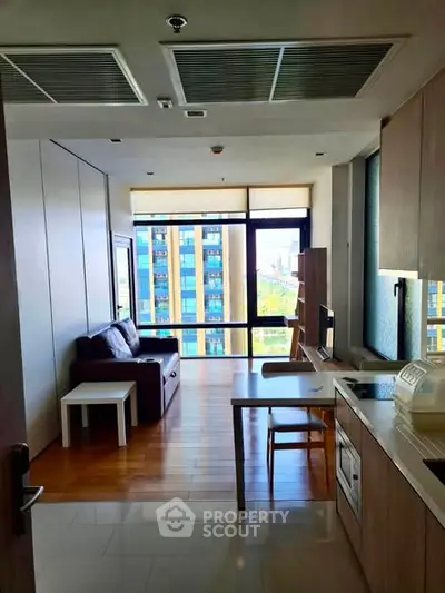 Modern living room with large windows and city view, featuring a cozy sofa and sleek kitchen area.
