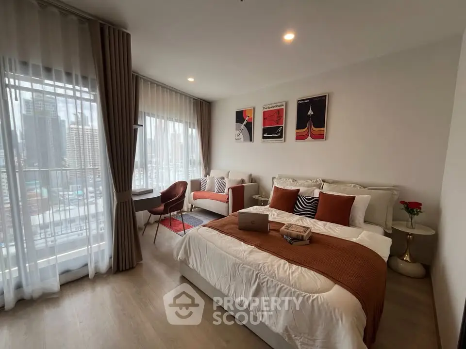 Modern bedroom with city view, stylish decor, and cozy seating area in a high-rise apartment.