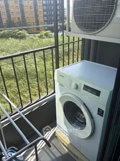 Cozy balcony with washing machine and air conditioning unit overlooking green space.