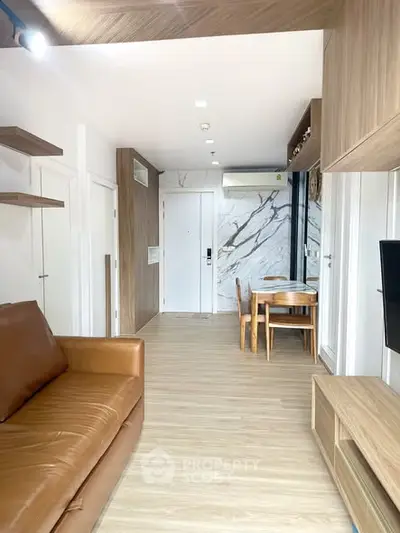 Modern living room with wooden flooring, brown leather sofa, and dining area with marble accent wall.